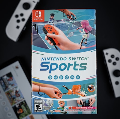 A box of Nintendo Switch Sports is prominently featured, surrounded by various Nintendo Switch controllers and a screen displaying a related interface. The box art depicts animated characters playing sports, such as tennis, with vibrant colors and action-oriented poses.